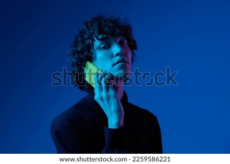 Man with phone in hand talking on smartphone, portrait dark blue background, neon light, style and trends, mixed light, men's fashion, copy place