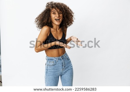 Beautiful woman with curly hair posing on a white isolated background smile happiness in jeans and black top emotion, hand signs, copy space