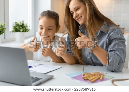 A teenage girl and her mother are happy with the teacher for an online homework consultation. Mom and daughter show thumbs up. Distant education concept. Selective focus.