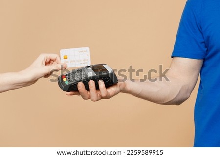 Close up cropped delivery guy employee man hold in hand hold bank payment terminal to process acquire credit card isolated on pastel plain light pastel beige wall background. Copy space advertising Royalty-Free Stock Photo #2259589915