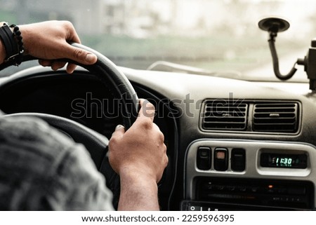 close-up of a latin man's hands, holding the steering wheel, while driving with a beautiful sunset in the background. Royalty-Free Stock Photo #2259596395