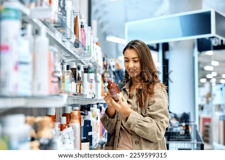 Young happy woman reading ingredients of skin care product while shopping at the store. Royalty-Free Stock Photo #2259599315
