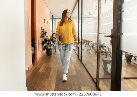 Businesswoman carrying laptop walking through hallway going to leave office after workday, full lengths portrait of cheerful confident freelance woman walking in modern coworking space Royalty-Free Stock Photo #2259608675