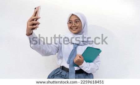 Indonesian female high school students in gray and white uniforms taking a selfie and holding a notebook