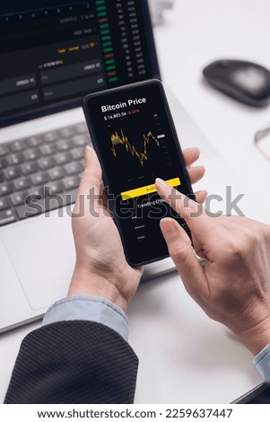 Broker or investor or cryptotrader using a smartphone application looks at financial data on the price of the stock market on a mobile phone, buys cryptocurrency.
