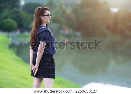 Happy Relaxing Portrait asian woman Wear dark blue dress while stand on green grass lawn beside a reservoir at the city park outdoors.