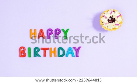 Happy Birthday. Greeting card. Multicolored plasticine letters near cake with pink candles. Copy spase. Light purple background.