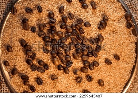 Coffee beans on brown sugar cane, lying on a bronze plate, against a background of coarse burlap. Background picture in brown tones