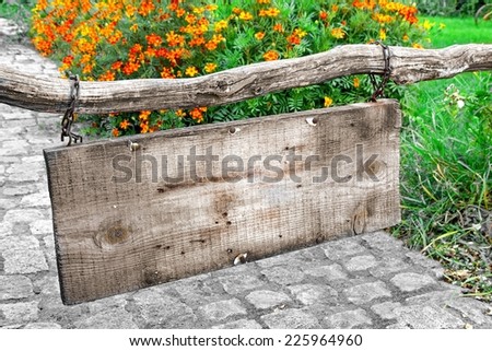 Empty Wood Hanging Signboard Closeup. In background stone pathway and flowers.