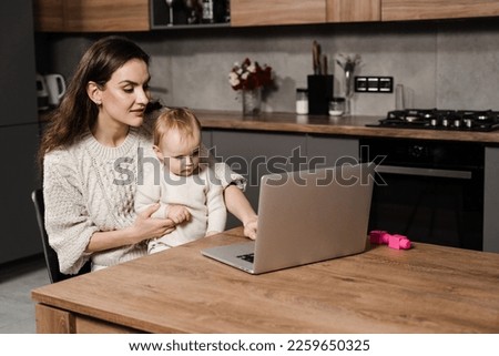 Family of mother and daughter toddler spending time together and watching videos online. Motherhood. Mom and child daughter are watching cartoons on laptop at home in the kitchen