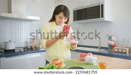 asian female photographer is using smart phone to take pictures in kitchen while she picking up the plate which has cake
