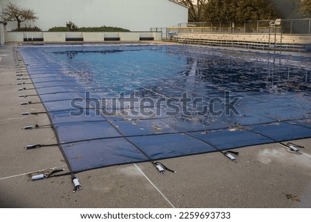 Swimming pool with cover from dirt. Public swimming pool with pool slide tarped up and closed down for winter. Pool with winter cover for autumn. Nobody, street photo