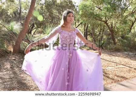 Close up portrait of beautiful young blonde model wearing a purple princess fantasy ball gown with flower crown diadem.
Pine forest location background with golden lighting.