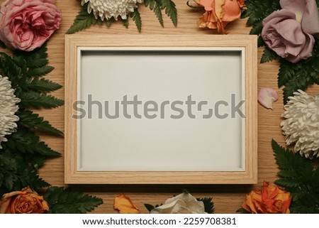 Wooden photo frame surrounded by fresh flowers and green leaves. Floral frame, spring or summer background