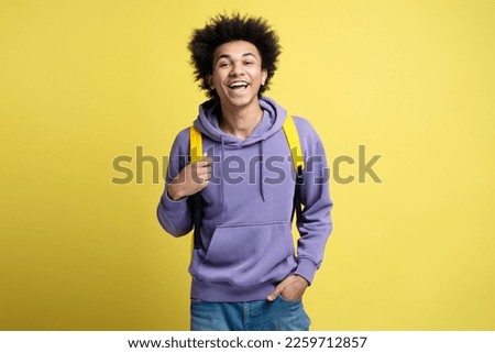 Smart smiling university student with backpack looking at camera isolated on yellow background. Education concept