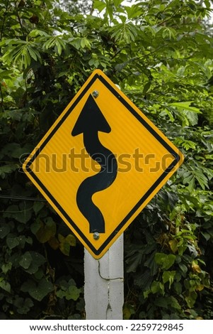 Yellow curves warning sign with green leaves in the background. Ko Lanta, Krabi, Thailand.