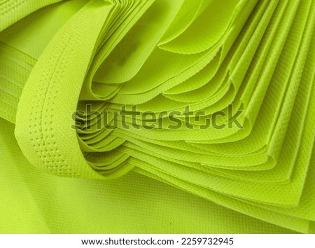pile of light yellowish green porous tote bags. non-woven fabric material. polypropyline bag