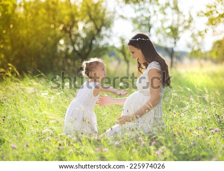 Cute little girl touching her mother's pregnant belly in summer nature