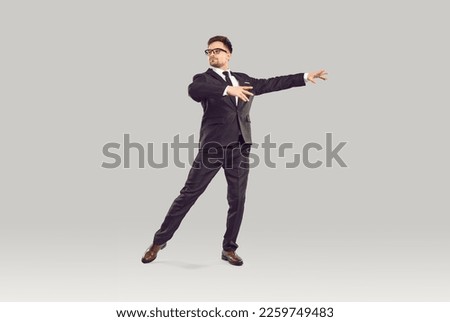 Serious office worker, corporate employee or businessman dancing in studio. Full body shot of handsome young business man in elegant suit, tie and glasses dancing alone isolated on grey background Royalty-Free Stock Photo #2259749483