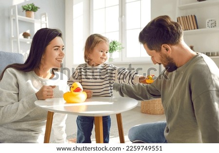 Little girl is having fun at home playing with toys with her loving mom and dad. Young Caucasian family with their little daughter spend time together sitting on floor in living room. Family concept.