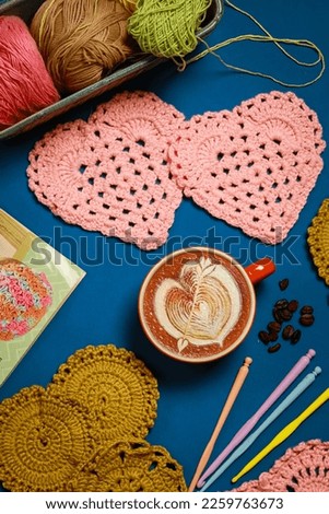 Cup of coffee and coasters crochet on blue background, top view.
