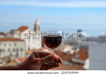 Hand with glass of ruby porto Portuguese wine in outdoor cafe at view point on colorful old part of Lisbon city, Portugal Royalty-Free Stock Photo #2259769999