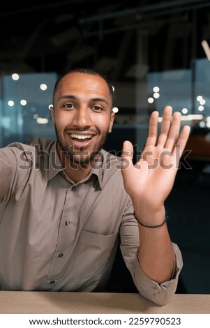Smiling and cheerful businessman in office taking selfie photo on phone and talking on video call with colleagues and friends using smartphone, african american man waving at camera greeting gesture. Royalty-Free Stock Photo #2259790523