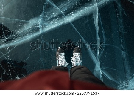 Feet in skates on the beautiful blue cracked ice of a frozen lake. Top view