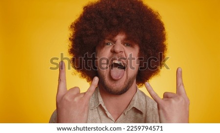 Rock n roll. Overjoyed delighted man with afro hairstyle showing gesture by hands, cool sign, shouting yeah with crazy expression, dancing, emotionally rejoicing in success win on yellow background