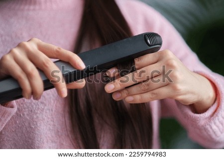 Woman straight hair using hair straightener. Hair ironing and hairstyle concept Royalty-Free Stock Photo #2259794983