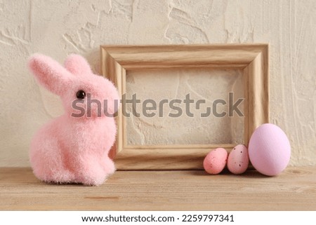 Empty picture frame, painted Easter eggs and bunny on wooden table near light wall