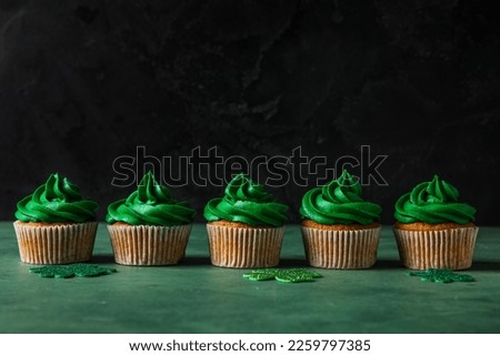 Tasty cupcakes for St. Patrick's Day on green table against black background