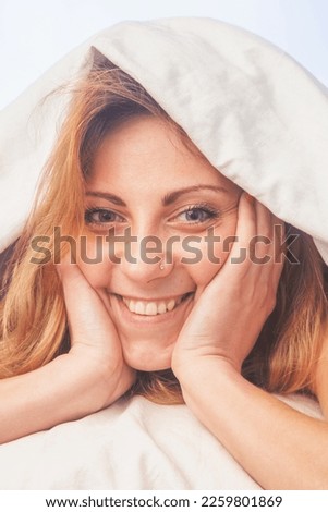 Conceptual image: good happy morning. Young girl lying in bed under the blanket in the morning Vertical image.