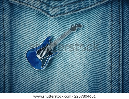 Vintage style blue guitar pin badge on denim biker jacket of a heavy metal rock music fan Royalty-Free Stock Photo #2259804651