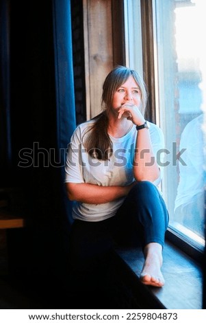 A young woman is sitting on the window and looking away.