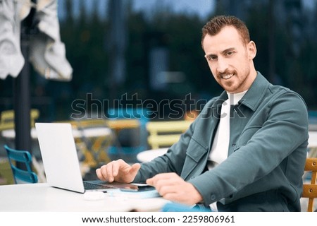 Successful confident freelancer using laptop computer, working online looking at camera sitting at street workplace. Successful business  concept 