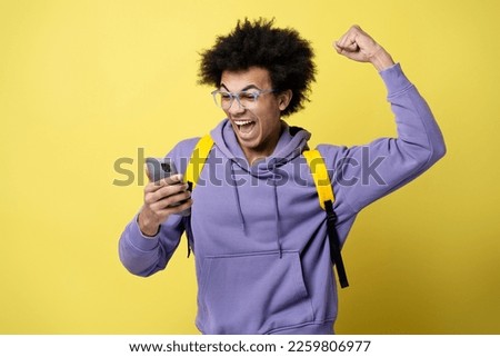 Young overjoyed African American man using smartphone playing mobile game celebration success isolated on yellow background. Emotional gambler sports betting, win money. Male shopping online with sale