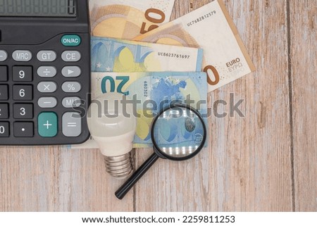 Light bulb, euro banknotes, magnifying glass. Rising electricity prices in Europe. Crisis of energy production in EU countries. Rising cost of electricity. Search for the cheapest electricity price
