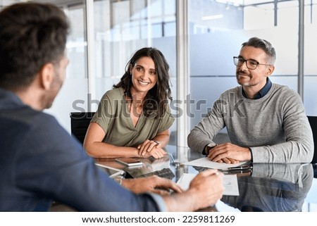 Smiling mature couple meeting with bank manager for investment. Mid adult woman with husband listening to businessman during meeting in conference room. Middle aged couple meeting loan advisor. Royalty-Free Stock Photo #2259811269