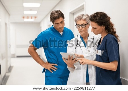 Mature female doctor discussing medical report with nurses in hospital hallway. Senior general practitioner discussing patient case status with group of medical staff after surgery. Doctors working. Royalty-Free Stock Photo #2259811277