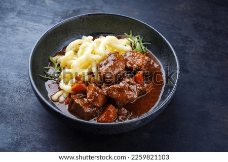 Traditional Hungarian braised venison goulash with vegetable and spaetzle in spicy sauce served as close-up in a Nordic design bowl  Royalty-Free Stock Photo #2259821103
