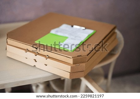 Cardboard pizza boxes with delivery clipboard on kitchen in table.