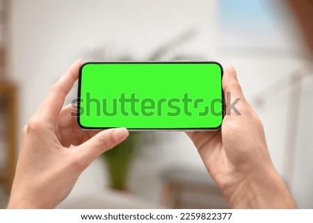 Woman holding smartphone with green screen indoors, closeup. Gadget display with chroma key. Mockup for design