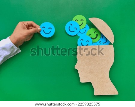 Hands adding smile symbols to people's head symbols. on a green background paper cut smiley face put in the head symbol Positive Concepts on Mental Health and World Mental Health Day