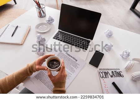 Top view of freelancer holding cup of coffee near devices and papers with copywriting lettering on table