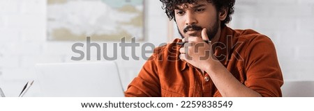 Focused indian freelancer looking at laptop at home, banner