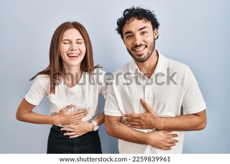 Young couple wearing casual clothes standing together smiling and laughing hard out loud because funny crazy joke with hands on body. 