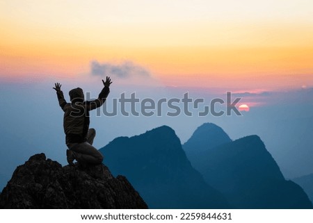Silhouette Man kneeling down with hands open palm up praying to God on top mountain sunset background. Royalty-Free Stock Photo #2259844631