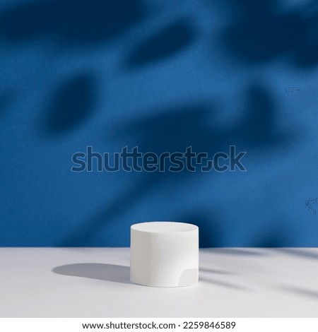 Empty white round podium and shadows on dark blue background. Showcase for product presentation. Pedestal for beauty cosmetic advertising. Minimal still life. Front view. Square photo.