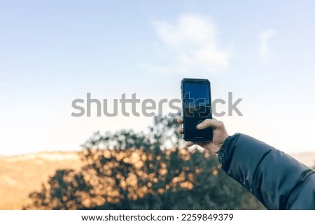 hand of young digital nomad adventurer taking a picture with his smart phone to a mountainous landscape during a clear sunset horizontal